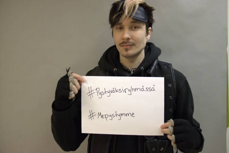 Opiskelija pitää kädessään paperia,josaa lukee #Pystyväksiryhmässä ja #Mepystymme
