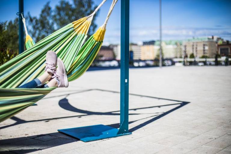 Hiekkakentällä riippumatto, jossa loikoilevan henkilön jalat näkyvissä.