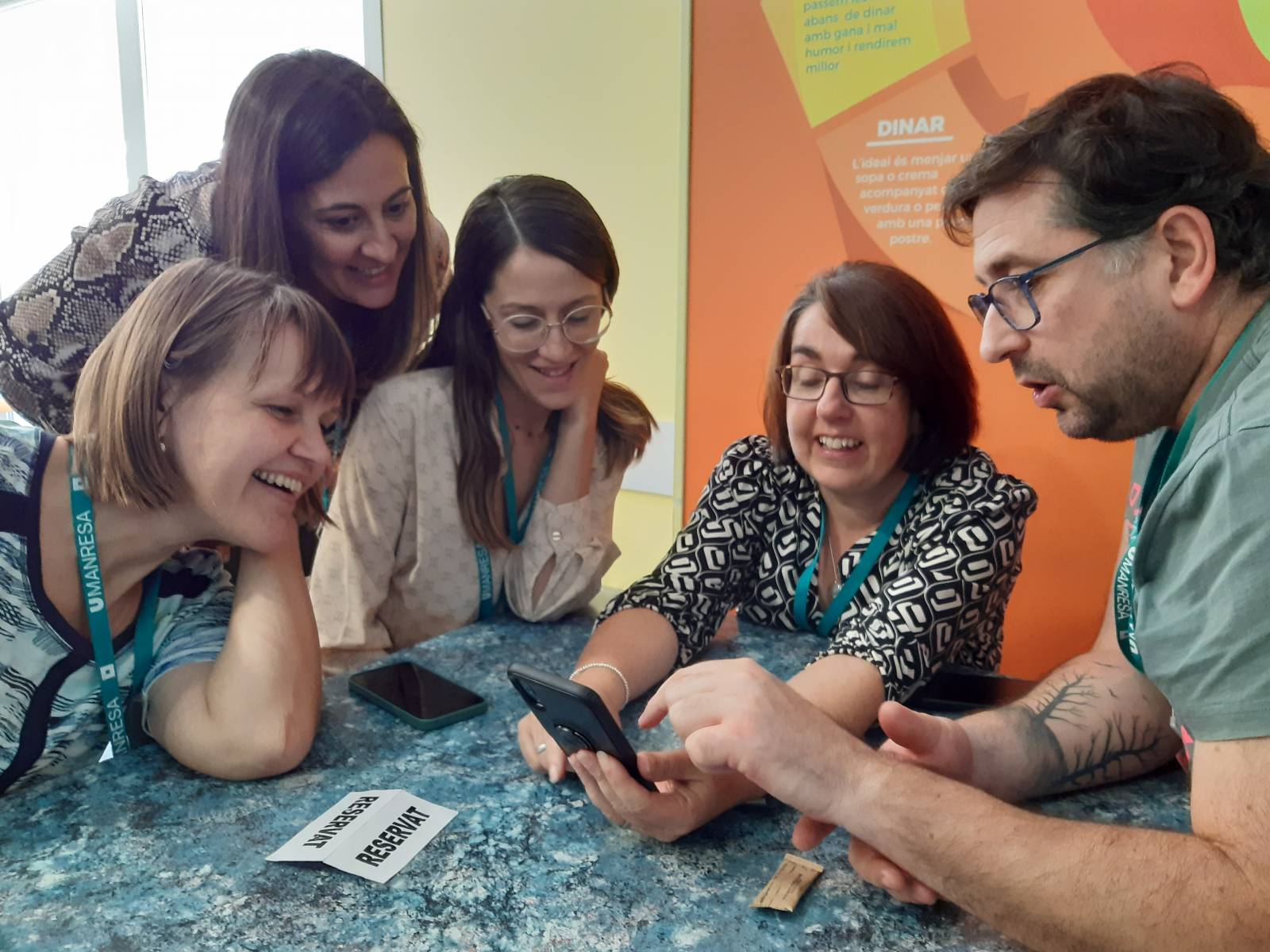 Five people looking at the phone and smiling.