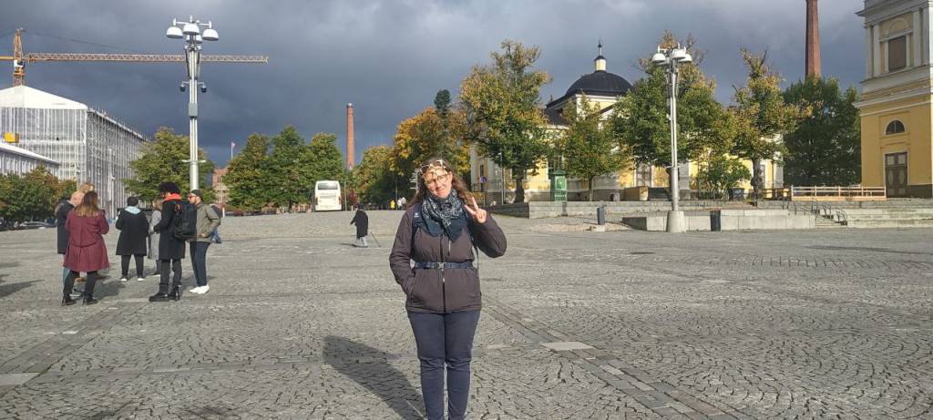 A female person doing a peace sign who is standing on a big square
