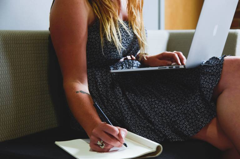 A woman working on a laptop and writing on her notebook