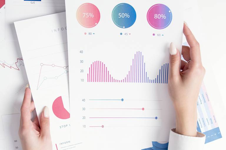 Naisen kädet pitelevät paperia, jossa on talouteen liittyviä graafeja.