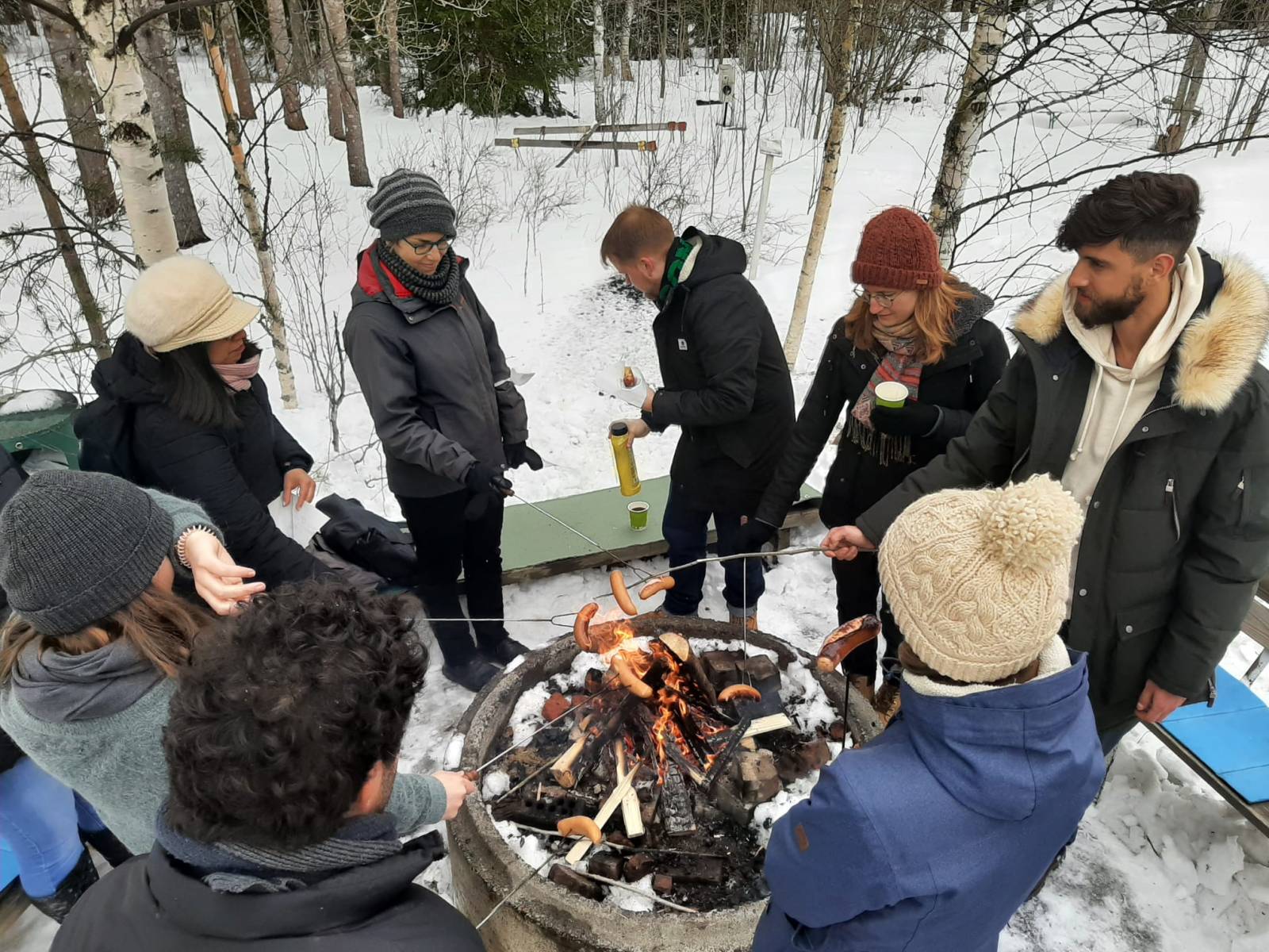People frying sausages on campfire.