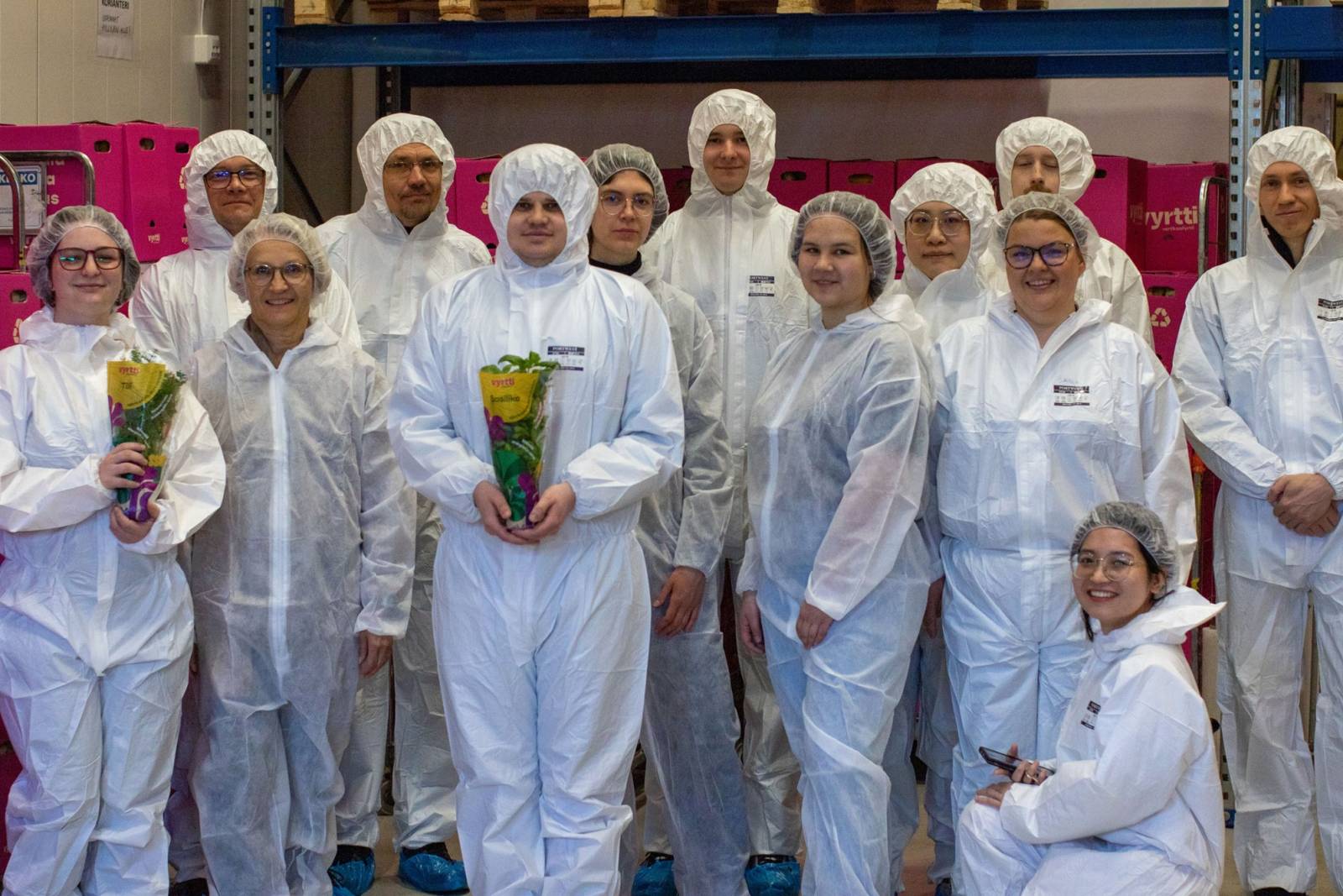 Thirteen people in a group with white protective overalls on.