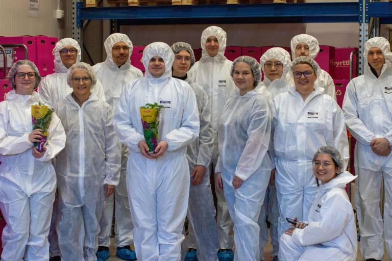 Thirteen people in a group with white protective overalls on.