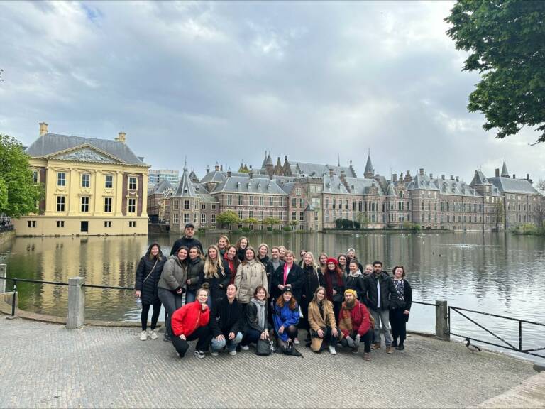 Ihmisiä ryhmämuodostelmassa, taustalla vettä ja rakennuksia.