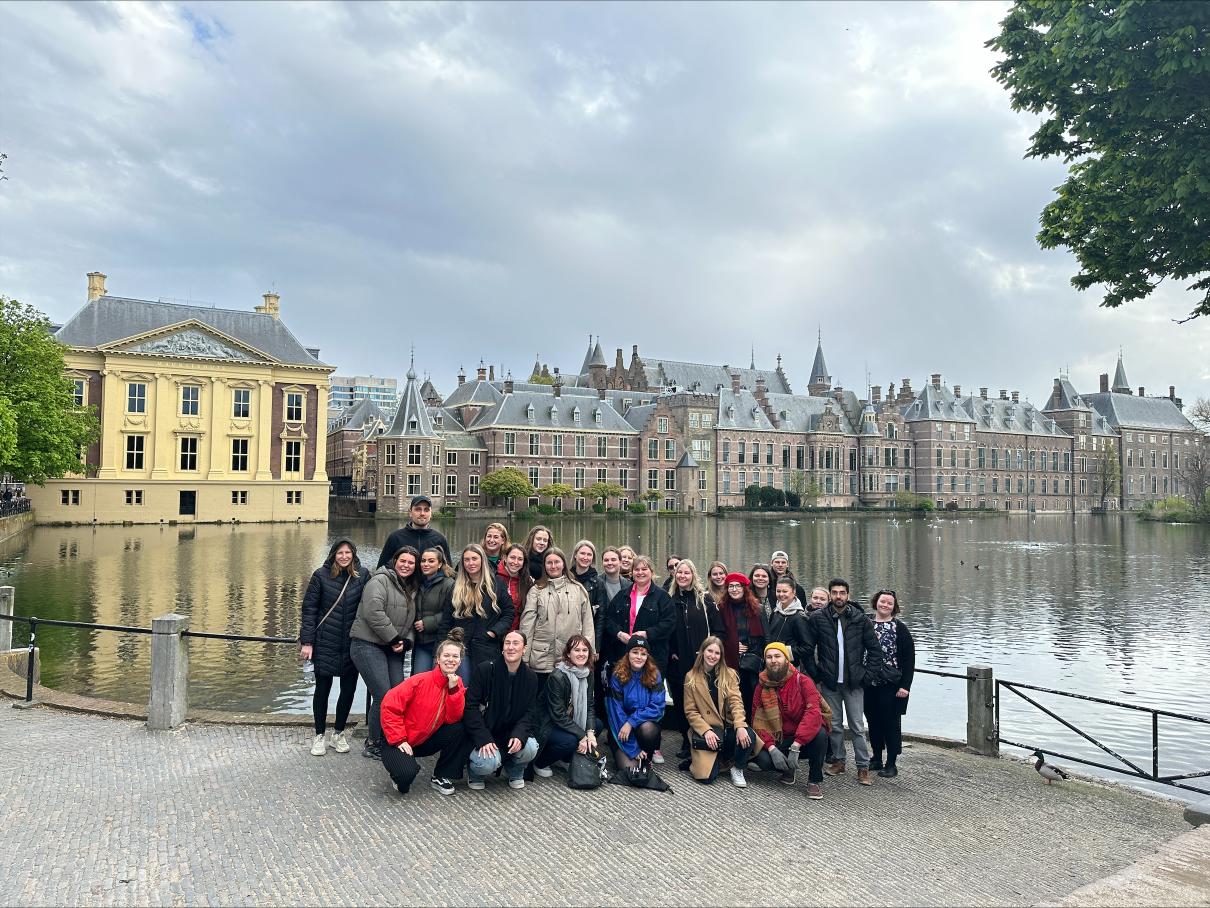 Ihmisiä ryhmämuodostelmassa, taustalla vettä ja rakennuksia.