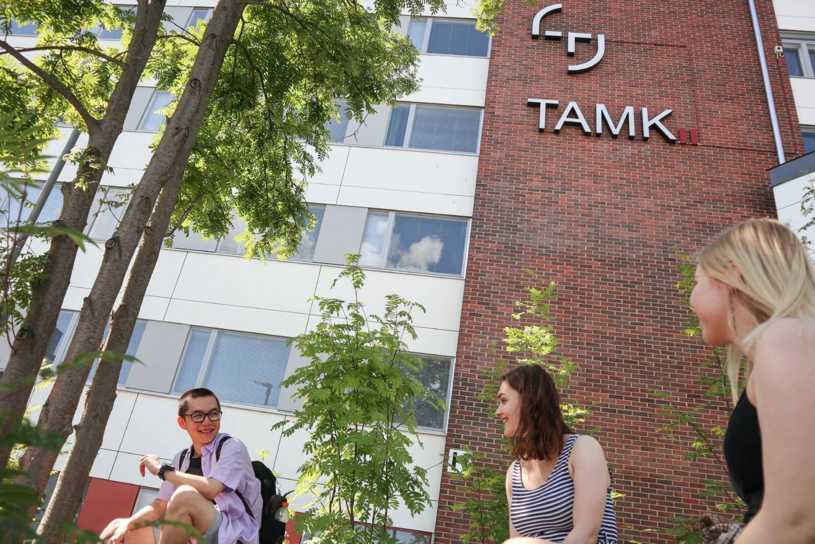 Kolme opiskelijaa Tamkin päärakennuksen edessä kesällä.
