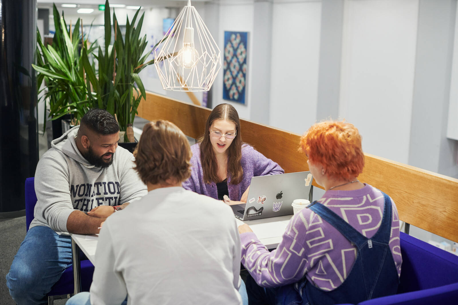 Neljä opiskelijaa istumassa pöydän ääressä ja tekemässä ryhmätyötä