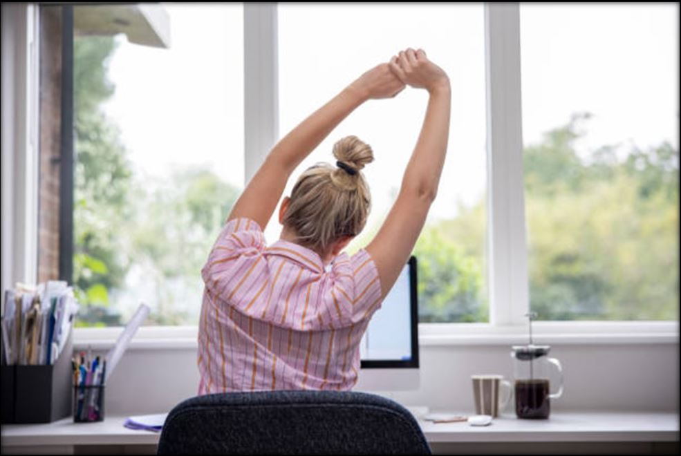 Nainen venyttelee läppärillä työskentelyn lomassa.