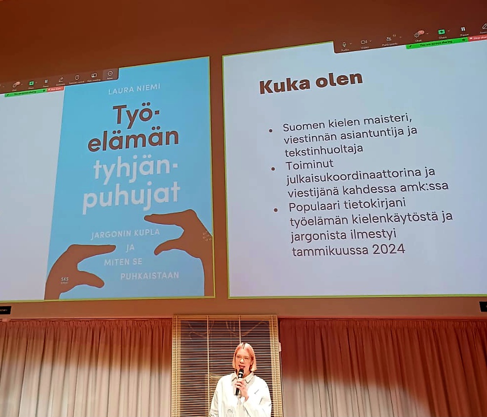 Nainen puhumassa lavalla mikrofoniin.