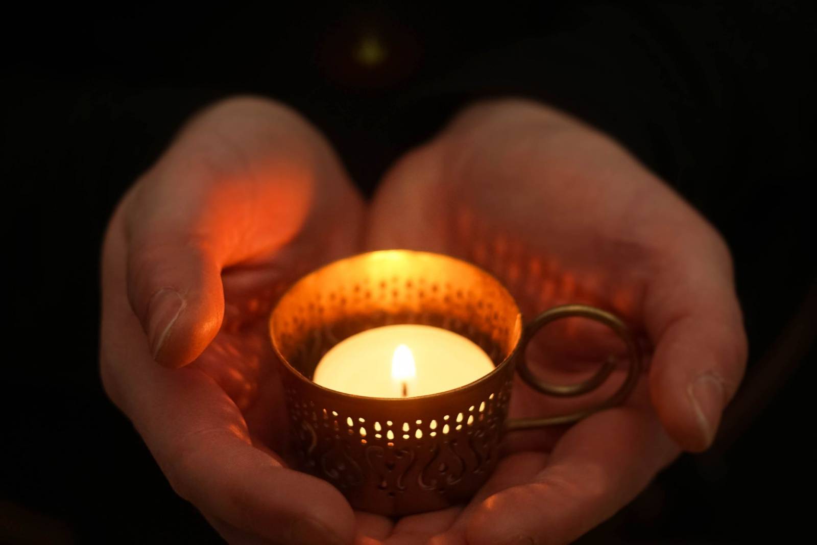 Tuikkukynttilä kämmenillä, jotka muodostavat sydämen kynttilän ympärillle.