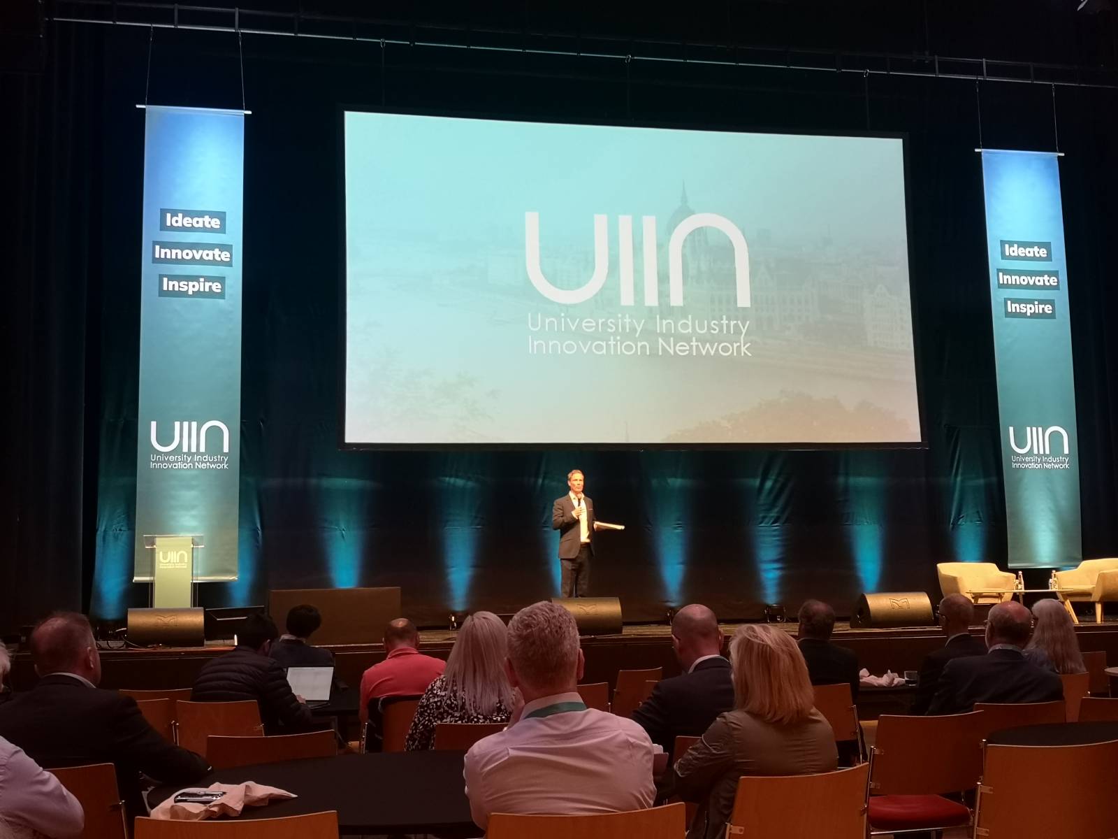 A man standing on a stage while the audience is listening to him.