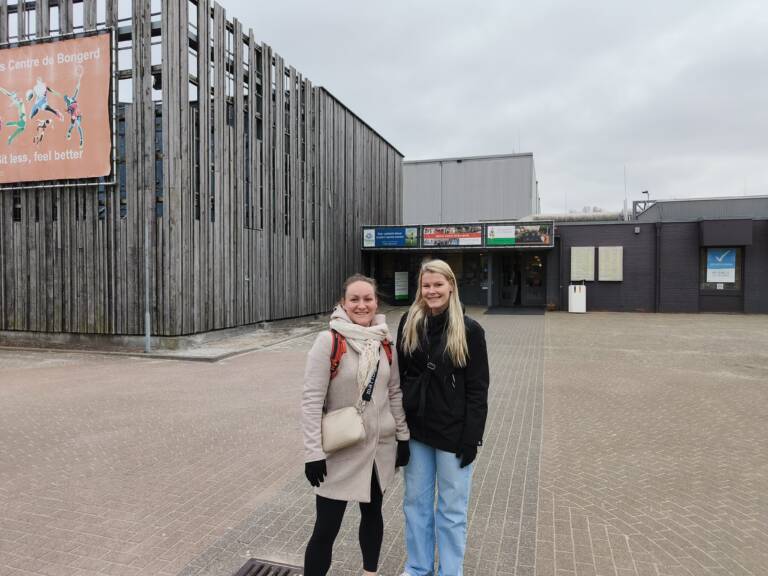 Kaksi naista seisomassa ulkona ison rakennuksen vieressä.