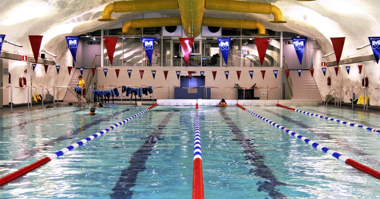 A picture of the swimming pool inside of the building. There are some people swimming, but itherwise, the pool is not crowded.