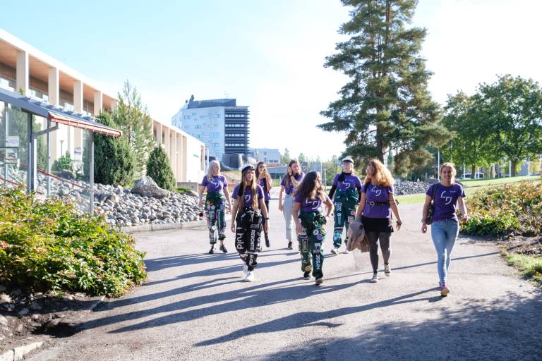 A group of students walking in Hervanta campus wearing purple Tampere University tshirts