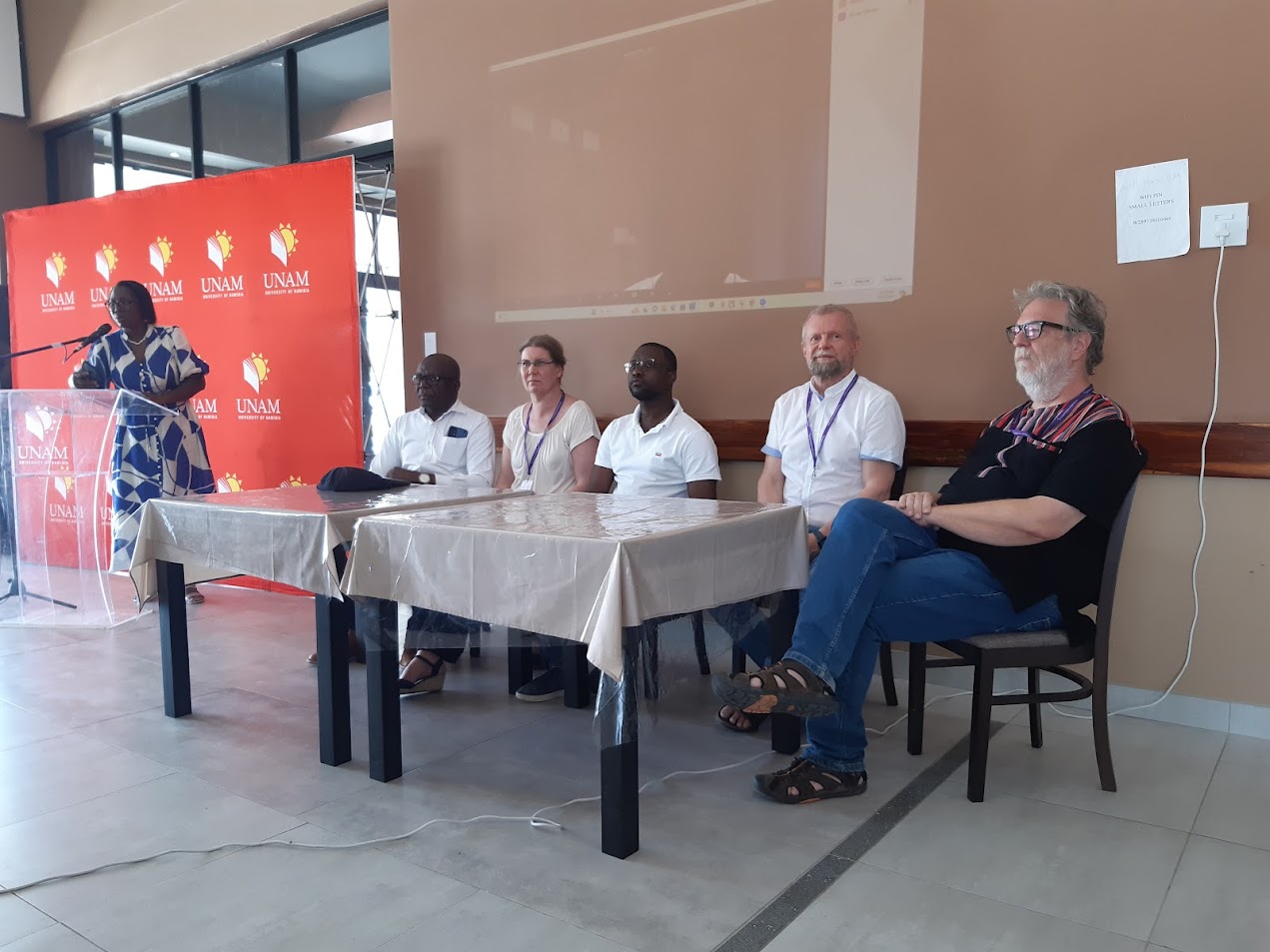 Viisi ihmistä istumassa kahden pöydän takana.