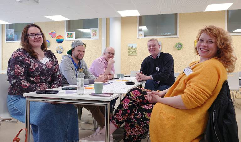 Viisi henkilöä kerääntyneenä pöydän ympärille.