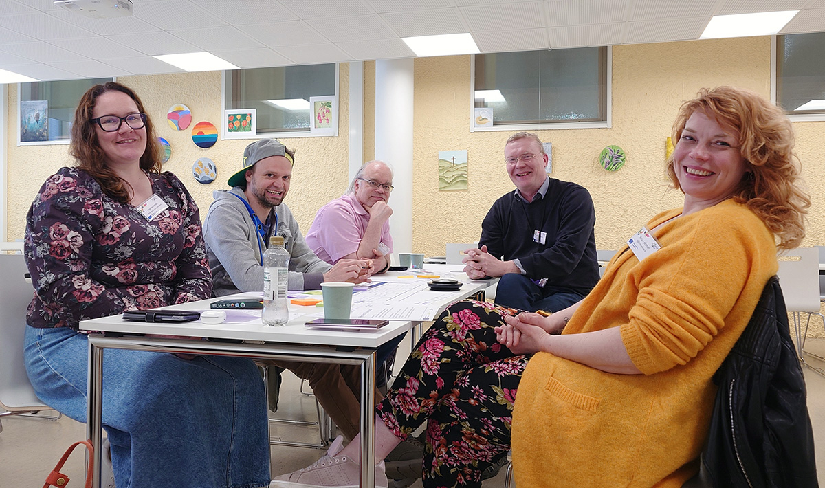 Viisi henkilöä kerääntyneenä pöydän ympärille.