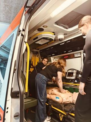 Opiskelijoita harjoittelemassa elvytysnukella ambulanssissa.
