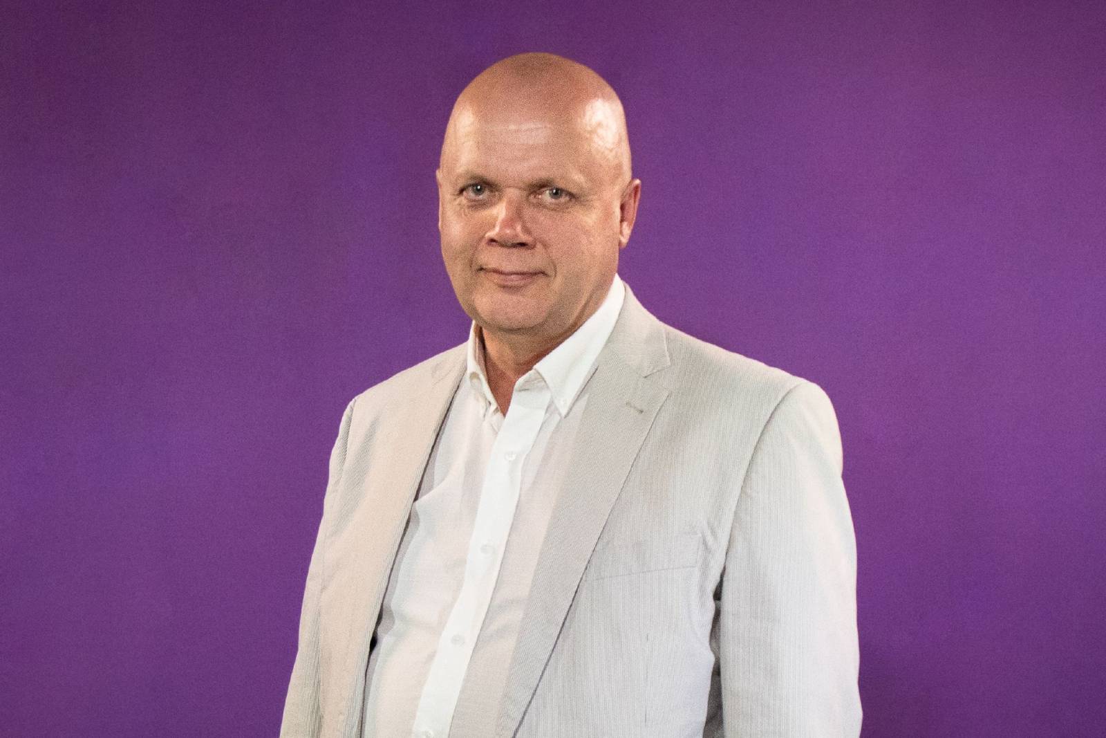 Kalju mies vaaleassa puvussa hymyilee kameralle