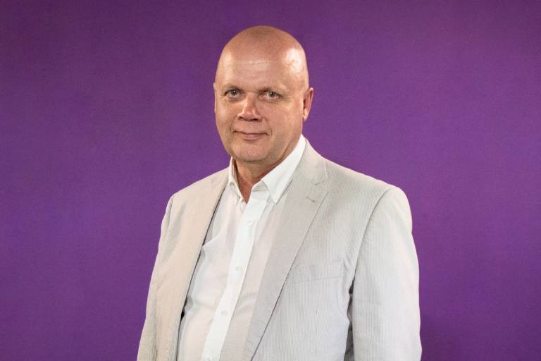 Kalju mies vaaleassa puvussa hymyilee kameralle