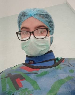 Henkilö pukeutuneena hiussuojaan, maskiin, sädesuojiin ja steriiliin takkiin