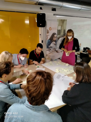 Ihmisiä istumassa pöydän ympärillä tehden ryhmätehtävää.