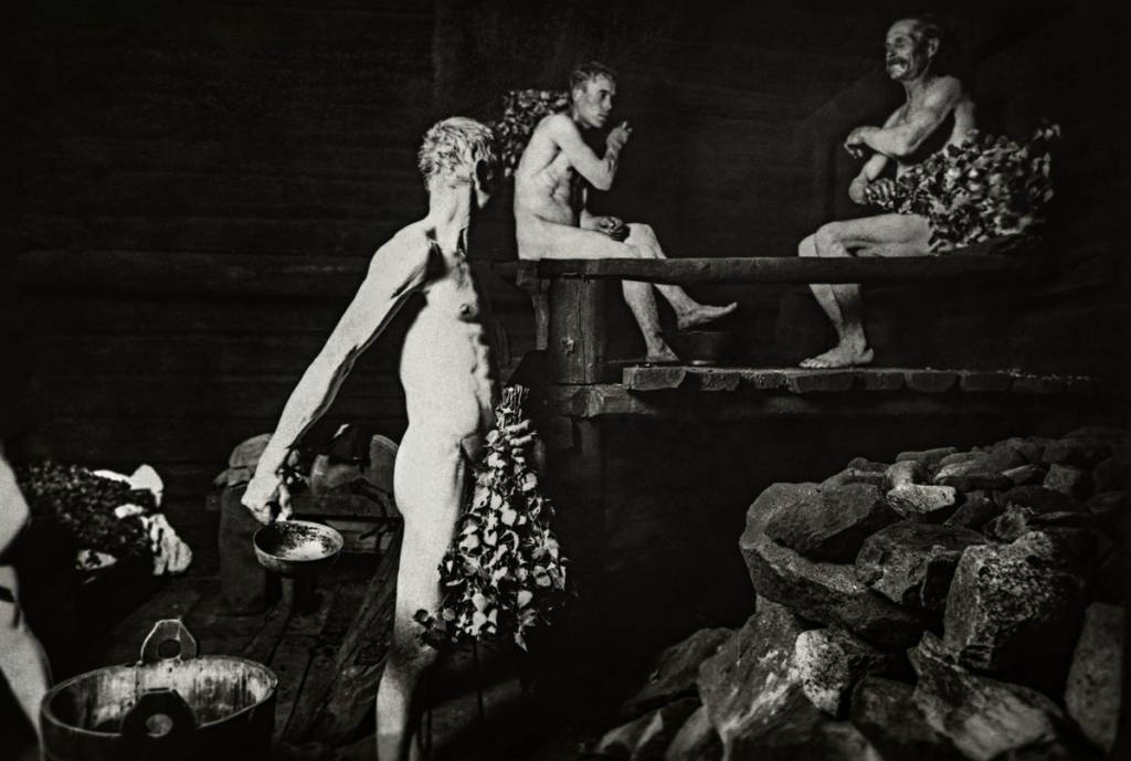 Mustavalkoinen vanha valokuva, jossa kolme miestä kylpee saunassa.